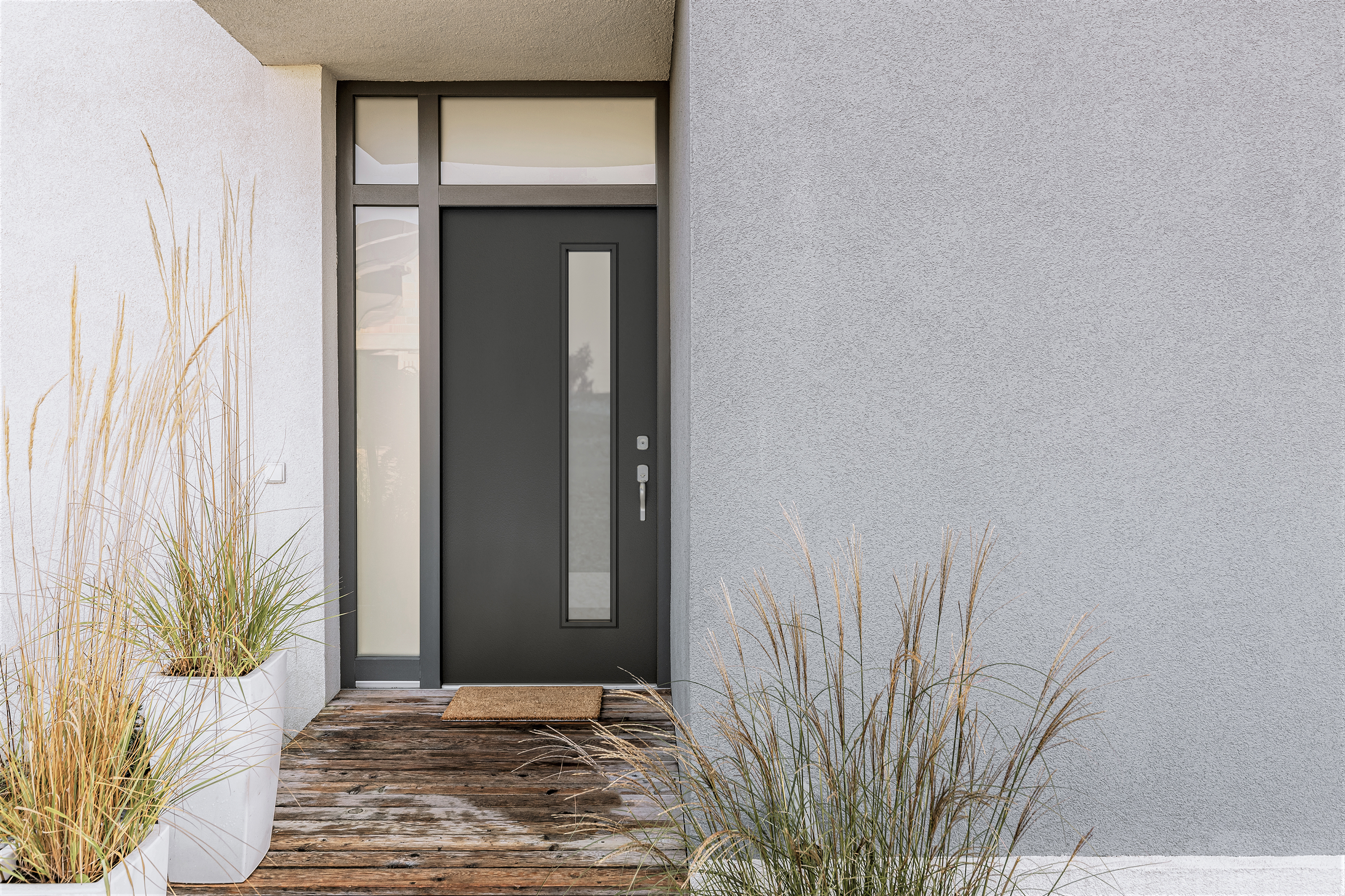 the outside of a modern-style home with gray exterior walls and a black front door with a single skinny glass pane on the right and one sidelite on the left