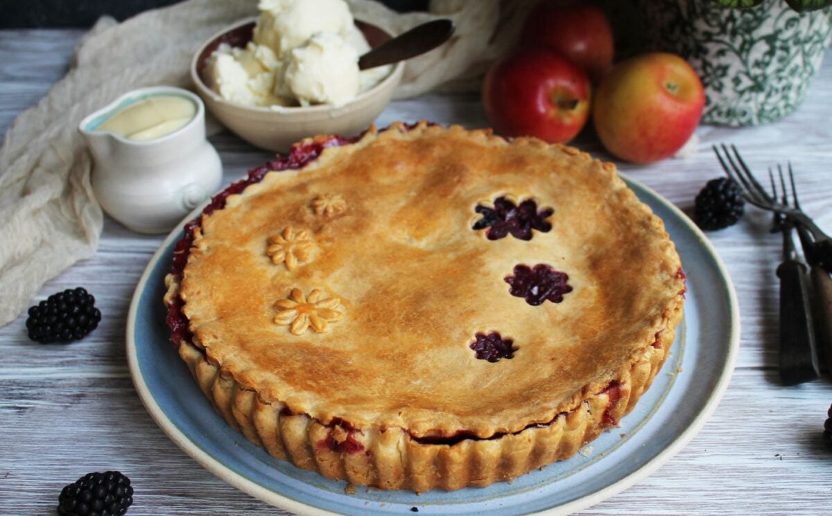 A vegan apple and blackberry pie next to some dairy-free cream and ice cream