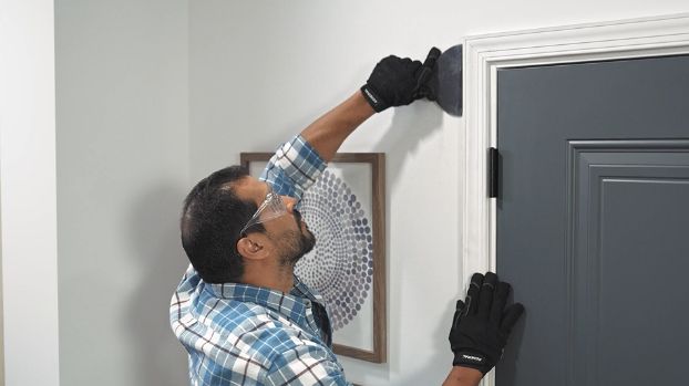 man-using-a-wide-putty-knife-to-separate-door-casing-and-wall